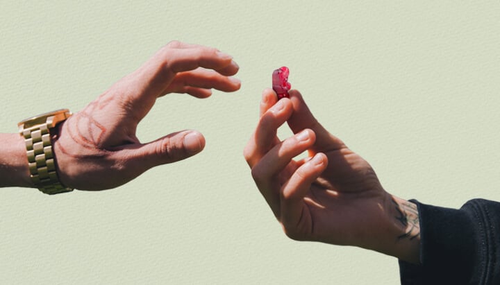 Twee handen reiken naar elkaar, één met een tatoeage, die een rode THC-gummybeer vasthoudt.