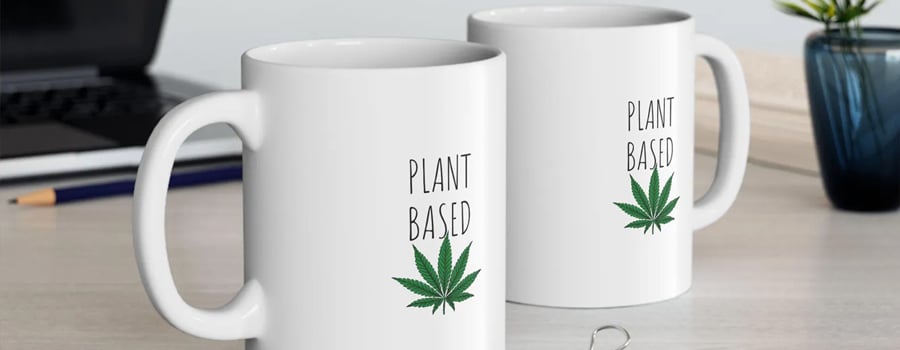 Twee witte mokken met de woorden "Plant Based" en een groene marihuanablad erop gedrukt.