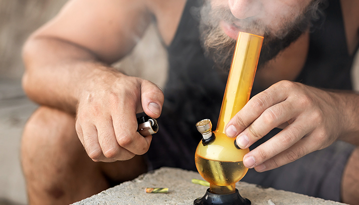 Persoon die hasj rookt uit een glazen bong en dikke rook uitademt.